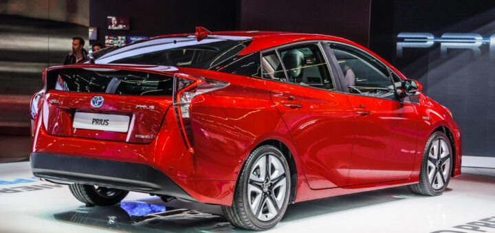 Red Toyota Prius displayed at an indoor auto show, viewed from the rear passenger side.